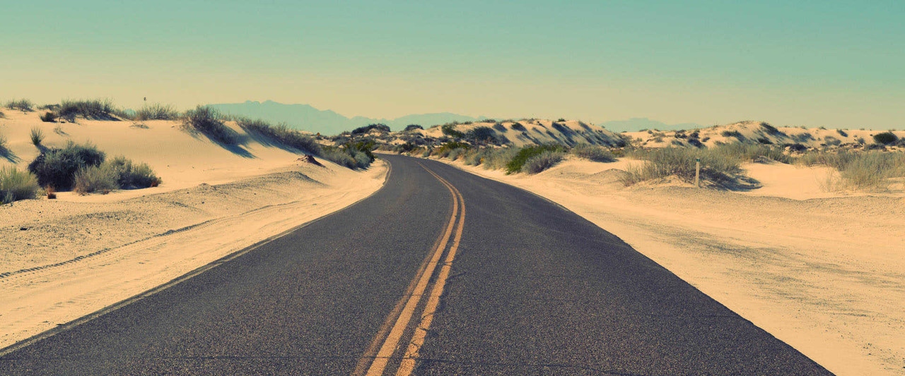 Desert road crossing dunes toward distant mountains